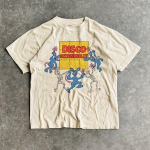 May include: Cream-colored t-shirt featuring a graphic design with the words "DISCO OCCASIONALLY" in a yellow square. The design includes blue cartoon rabbits and skeleton figures dancing. The shirt has short sleeves and a crew neck.