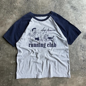May include: A gray and navy blue raglan t-shirt featuring a graphic print of a person running away from a small dog. The text "dog power" and "running club" is printed in navy blue ink on the front of the shirt, which has short sleeves.
