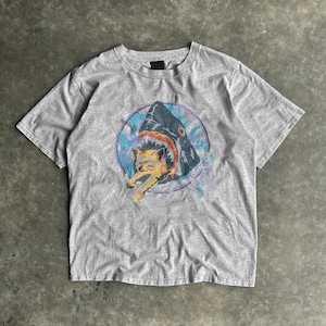 May include: A grey t-shirt with a graphic print of a shark biting a cat. The shark is dark blue with a red mouth, and the cat is orange and yellow. The graphic is set within a blue and purple circle.