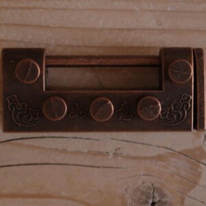 May include: A rectangular, antique-style copper-toned metal latch featuring a horizontal bar, three circular decorative accents, and engraved cloud motifs on the sides. The hardware includes visible screw heads and subtle Chinese characters.