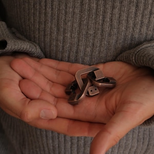 May include: A metallic copper-coloured puzzle consisting of several interlocking geometric pieces with smooth edges and small circular indentations on the surface. The object is composed of multiple connected segments that form a complex, compact shape.