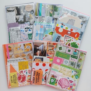 Peut inclure: Une collection d'autocollants colorés, d'éphémères en papier et de petits objets décoratifs disposés dans des pochettes en plastique transparent. Les articles comprennent des illustrations de nourriture, des motifs floraux et du texte japonais.