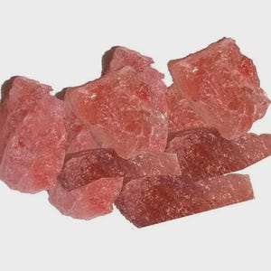 May include: A collection of rough-cut, translucent rose quartz crystals. The crystals vary in size and shape, displaying a range of pink hues from light to deep rose. The raw stones have a natural, unpolished appearance.