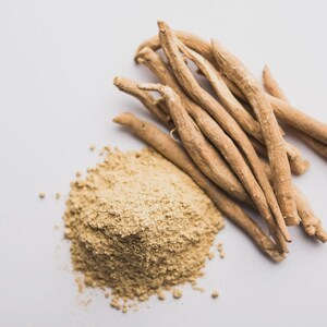 Op de afbeelding: Een close-up van lichtbruin ashwagandapoeder en wortels. Het poeder is fijn gemalen, naast een bundel beige ashwagandawortels. De wortels zijn lang en dun. De achtergrond is effen wit.