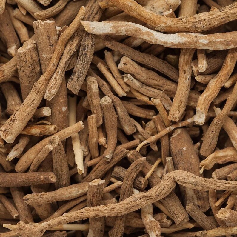 Op de afbeelding: Close-up van stukjes ashwagandha-wortel. De stukjes zijn verschillend van grootte en vorm, met een lichtbruine kleur en een ruwe textuur. Sommige stukjes hebben een lichtere, bijna witte buitenlaag. De afbeelding is goed belicht.