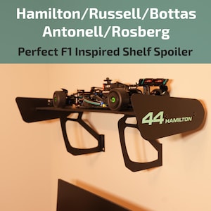 May include: Black shelf spoiler inspired by F1 design, mounted on a wall. The shelf holds a model race car. The spoiler features the number "44" and the name "HAMILTON" in green. The text "Hamilton/Russell/Bottas Antonell/Rosberg Perfect F1 Inspired Shelf Spoiler" is at the top.