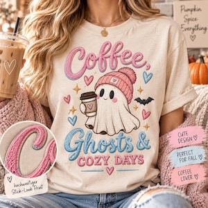 Op de afbeelding: Een crèmekleurig T-shirt met een afbeelding van een geest die een roze gebreide muts draagt en een koffiebeker vasthoudt. De tekst luidt Coffee, Ghosts & Cozy Days. Het ontwerp bevat kleine hartjes, sterren en een vleermuis. Een cirkelvormige inzet toont een close-up van de roze geborduurde letters.