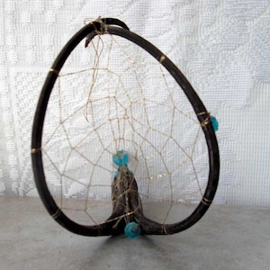May include: A dreamcatcher made from a natural branch with a woven web and blue beads.