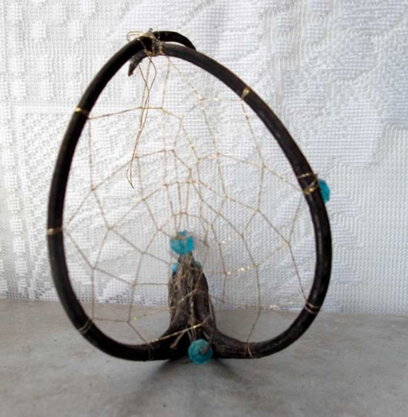 May include: A dreamcatcher made from a natural branch with a woven web and blue beads.