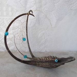 May include: A handmade dreamcatcher made from natural materials, featuring a curved wooden base, a delicate web of string, and turquoise beads.
