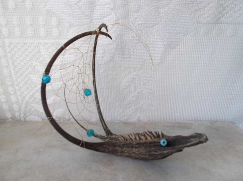 May include: A handmade dreamcatcher made from natural materials, featuring a curved wooden base, a delicate web of string, and turquoise beads.