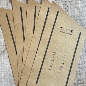 May include: A set of five rectangular tan paper cash envelopes arranged in a fan pattern. Each envelope features two vertical black lines and a printed section labeled AMOUNT WITHIN with a list of currency denominations including 10, 50, 25, 2, 1, 25 cents, 5 cents, 1 cent, 10 cents, 50 cents, 2, 5, and 10 dollars.