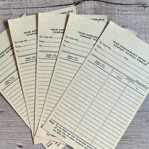 May include: A stack of vintage train baggage report forms. The forms are beige with black text and lines. The text includes "Train Baggage Company Material Handled" and "Serial No. Form S-121". The forms are slightly angled.