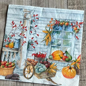 May include: A square paper napkin featuring a watercolor illustration of a harvest scene. The design includes a wooden cart filled with vegetables, a basket of red apples, pumpkins, corn, and red berries against a white wooden wall background.
