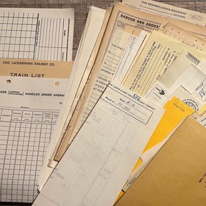 May include: A collection of vintage railway documents, including train lists, records of cars, and other forms. The papers are aged with a mix of handwriting and printed text, featuring logos and text like "Erie Lackawanna Railway Co." and "Train List."