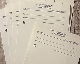 Puede incluir: Una pila de blocs de recetas blancos con el nombre impreso Marvin Freedman, M.D., 277 Sylvan Road, Glencoe, IL 60022, y DEA NO. AF 4589012. Cada bloc incluye líneas para For, Address, Date, el símbolo Rx y casillas de verificación para sustitución.