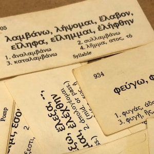 May include: A collection of vintage flashcards with Greek text and numbers. The cards are off-white with black text, and some have the word "Syllable" printed on them. The cards are arranged in a slightly overlapping pattern.
