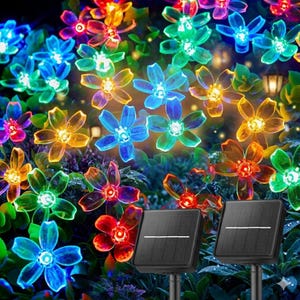 May include: Solar-powered flower lights in various colors, including blue, green, yellow, and red. The lights are arranged in a garden setting with two black solar panels in the foreground. The flowers have a translucent appearance.