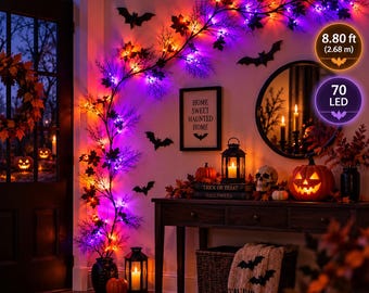 Może przedstawiać: Girlanda na Halloween o długości 2,68 m z 70 diodami LED, czarnymi gałązkami i liśćmi w jesiennych kolorach. Girlanda jest ozdobiona czarnymi wycinankami nietoperzy i wyeksponowana obok dyni, latarni oraz dekoracyjnej czaszki.