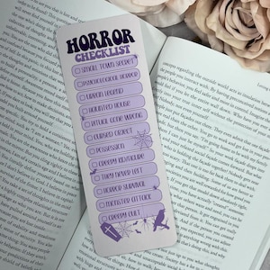 May include: A lavender bookmark with the words "HORROR CHECKLIST" in a stylized font. The checklist includes horror themes like "Small Town Secret" and "Creepy Cult." Decorative elements include a spiderweb, bats, a coffin, and a raven.