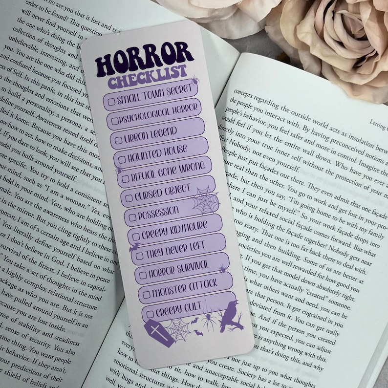 May include: A lavender bookmark with the words "HORROR CHECKLIST" in a stylized font. The checklist includes horror themes like "Small Town Secret" and "Creepy Cult." Decorative elements include a spiderweb, bats, a coffin, and a raven.