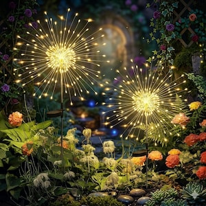 May include: Two solar-powered garden lights with a firework-like design. Each light features a central cluster of warm white LEDs with radiating wires, creating a starburst effect. The lights are set amidst a lush garden with flowers and greenery.