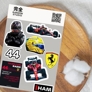 May include: A sheet of Formula 1 racing stickers featuring race cars, helmets, and team logos. The stickers include the number 44, the text "HAMILTON RADIO", and the text "SAINZ 1.4 BEHIND".
