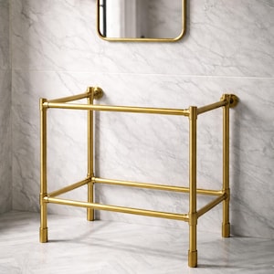 以下が含まれることがあります： 長方形のフレームの金色の金属製バスルームバニティスタンド。スタンドには下の棚があり、大理石模様の壁に取り付けられています。スタンドの上には金色のフレームの鏡があります。