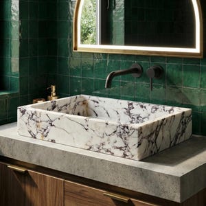 May include: A rectangular marble sink with a white base and dark purple veining sits on a concrete countertop. The sink is mounted above a wooden cabinet with brass handles. A black tap and mirror are mounted on a green tiled wall.