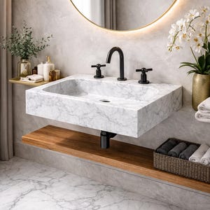 May include: A contemporary marble washbasin with black taps and fittings. The rectangular sink has a curved basin and is mounted on a wooden shelf. A gold-framed mirror and decorative items complete the bathroom setting.