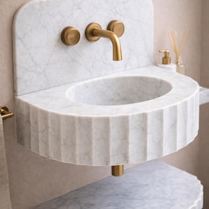 May include: A white marble wall-mounted sink with a fluted front design. The sink has a round basin and is paired with a gold-coloured faucet and fixtures. The design is minimalist and modern, suitable for a bathroom.