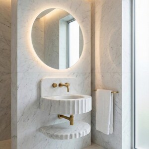 May include: A contemporary bathroom with a circular, illuminated mirror above a marble sink and brass taps. A matching marble shelf is below the sink. The walls are marble, and a towel hangs on a brass rail.