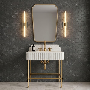 May include: A luxurious bathroom vanity set featuring a white marble sink with gold fixtures and a matching gold-framed mirror. The vanity is supported by a gold metal frame. The background features a dark gray hexagonal tile wall and two gold sconces.