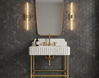 May include: A stylish bathroom vanity set with a white marble sink and gold taps, set against a dark grey hexagonal tile wall. The vanity has a gold frame, a matching gold-framed mirror, and two gold sconces. The overall design is elegant and modern.
