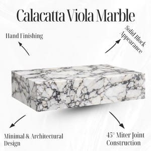 May include: A rectangular block of Calacatta Viola marble with a white base and dark gray veining. The image highlights the hand finishing, solid block appearance, minimal design, and 45&deg; miter joint construction. The text "Calacatta Viola Marble" is at the top.