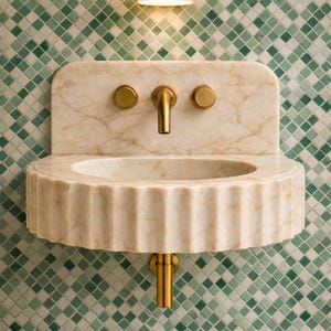 May include: A marble wall-mounted sink with a fluted basin and a marble backsplash. It features a gold tap and two gold knobs. The background is a mosaic tile pattern in shades of green and white.