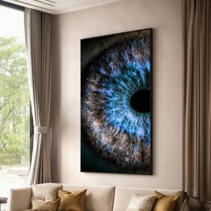 Puede incluir: Una impresión enmarcada de un ojo humano, que muestra detalles intrincados. El iris presenta tonos azules y marrones, con una pupila negra en el centro. La obra de arte se exhibe en un salón, añadiendo un toque de arte moderno.