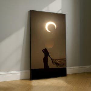 Può includere: Una stampa artistica incorniciata con la silhouette di una persona che tiene un tessuto fluente, con una luce a forma di mezzaluna nel cielo. L'opera d'arte è nei toni del marrone e del nero, appoggiata a un muro con pavimento in legno.