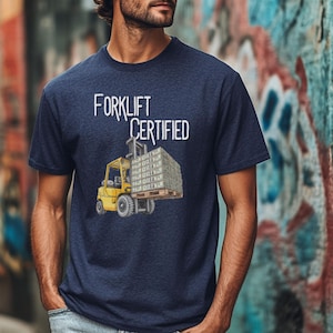 May include: Navy blue t-shirt with the words "FORKLIFT CERTIFIED" in white. The graphic shows a yellow forklift lifting a pallet of money. The shirt is made of a soft, comfortable material.