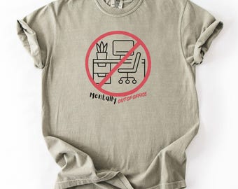 May include: A light olive green t-shirt featuring a graphic of a desk, computer, and chair inside a red circle with a line through it. The text "Mentally Out of Office" is below the graphic.
