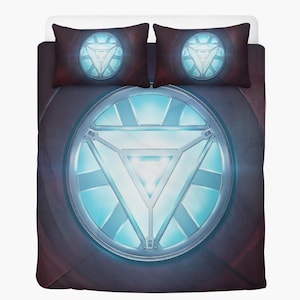 Może przedstawiać: Zestaw pościeli z dużym, świecącym niebiesko-białym trójkątnym wzorem na ciemnym tle. Zawiera dwie pasujące poszewki na poduszki. Wzór przypomina emblemat superbohatera. Zestaw jest przeznaczony do łóżka.