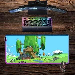 May include: A gaming setup featuring a curved monitor, a backlit mechanical keyboard, and a large mousepad with a colorful cartoon scene. A matching gaming mouse is also visible. The setup is placed on a wooden surface.