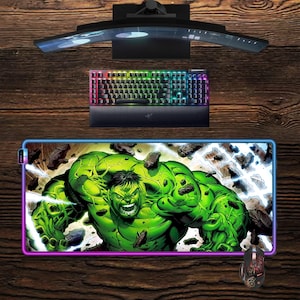 Könnte beinhalten: Gaming-Setup mit einem gebogenen Monitor, einer Tastatur mit Hintergrundbeleuchtung und einem Hulk-Mauspad und einer Maus. Das Mauspad hat einen lebendigen Rand und eine Grafik von Hulk, der durch Stein bricht.
