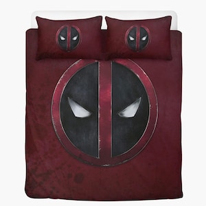 May include: A burgundy-colored bedding set featuring the Deadpool logo. The set includes a duvet cover and two pillowcases. The logo is a large, black and red circular design with white eye shapes. The bedding has a distressed, textured appearance.