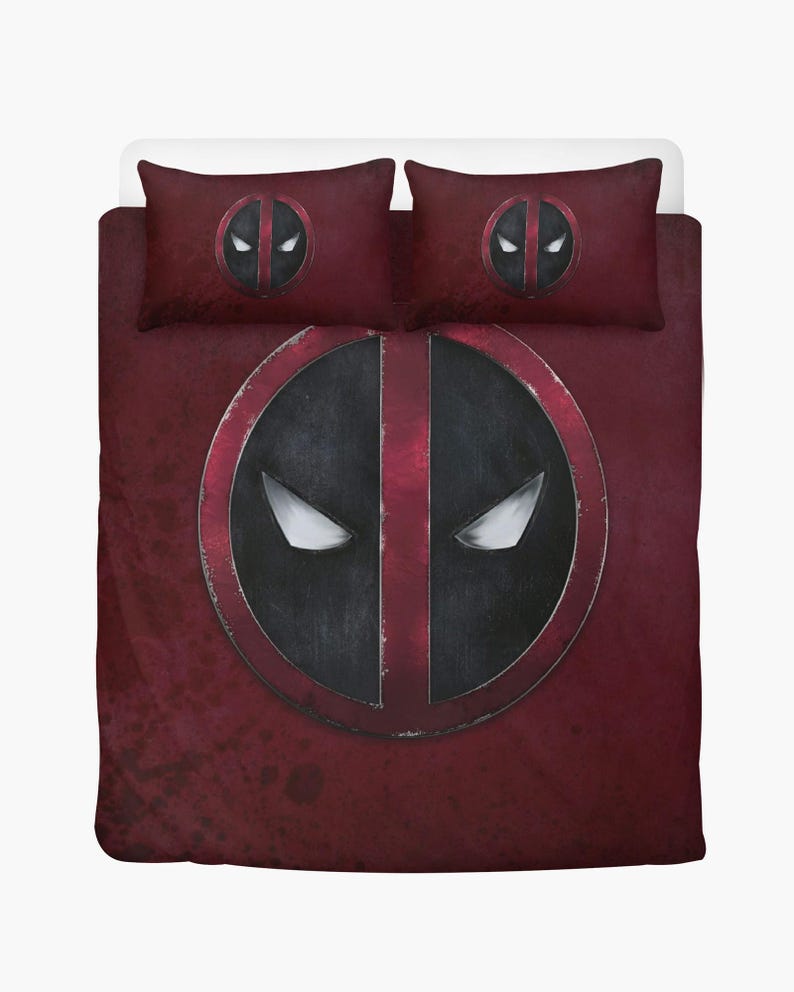 May include: A burgundy-colored bedding set featuring the Deadpool logo. The set includes a duvet cover and two pillowcases. The logo is a large, black and red circular design with white eye shapes. The bedding has a distressed, textured appearance.