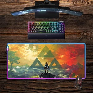 Peut inclure: Un ensemble de jeu comprenant un écran incurvé, un clavier rétroéclairé et une souris. Un grand tapis de souris rectangulaire avec un paysage coloré et une figurine avec une épée est également présent. L'ensemble est sur une surface en bois.