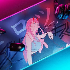 Może przedstawiać: Podkładka pod mysz do gier z ilustracją w stylu anime dziewczyny z różowymi włosami i rogami. Podkładka ma niebieską i różową obwódkę LED, z czarną myszą, kontrolerem i słuchawkami. Tekst "Darling in the" jest częściowo widoczny.
