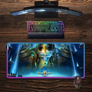 May include: A gaming setup featuring a curved monitor, a backlit keyboard, and a large mousepad. The mousepad displays a Starcraft graphic with a blue and gold color scheme. A gaming mouse is also visible.