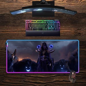 Pode incluir: Uma configuração de jogos com um monitor curvo, um teclado retroiluminado e um rato. Também está presente um tapete de rato retangular grande com um design de personagem de fantasia e uma borda brilhante. O teclado e o rato têm iluminação RGB.