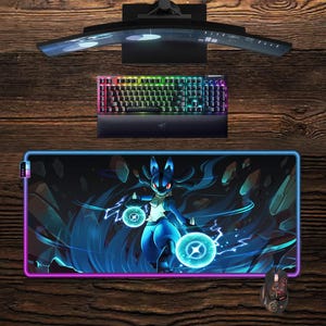 Op de afbeelding: Een gaming setup met een gebogen monitor, een regenboogverlicht toetsenbord en een grote muismat met een blauwzwarte afbeelding van Lucario. Een bijpassende muis is ook zichtbaar.